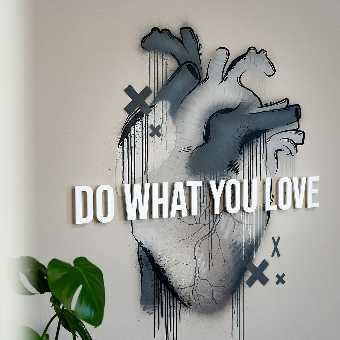 Ein anatomisches Herz, monochrom in warmem Grau, drei Elemente in kaltem, dunklem Grau. Urbaner Stil gemischt mit Acrylinstallation; diese ist als „Do what you love“-Schriftzug mittig platziert.